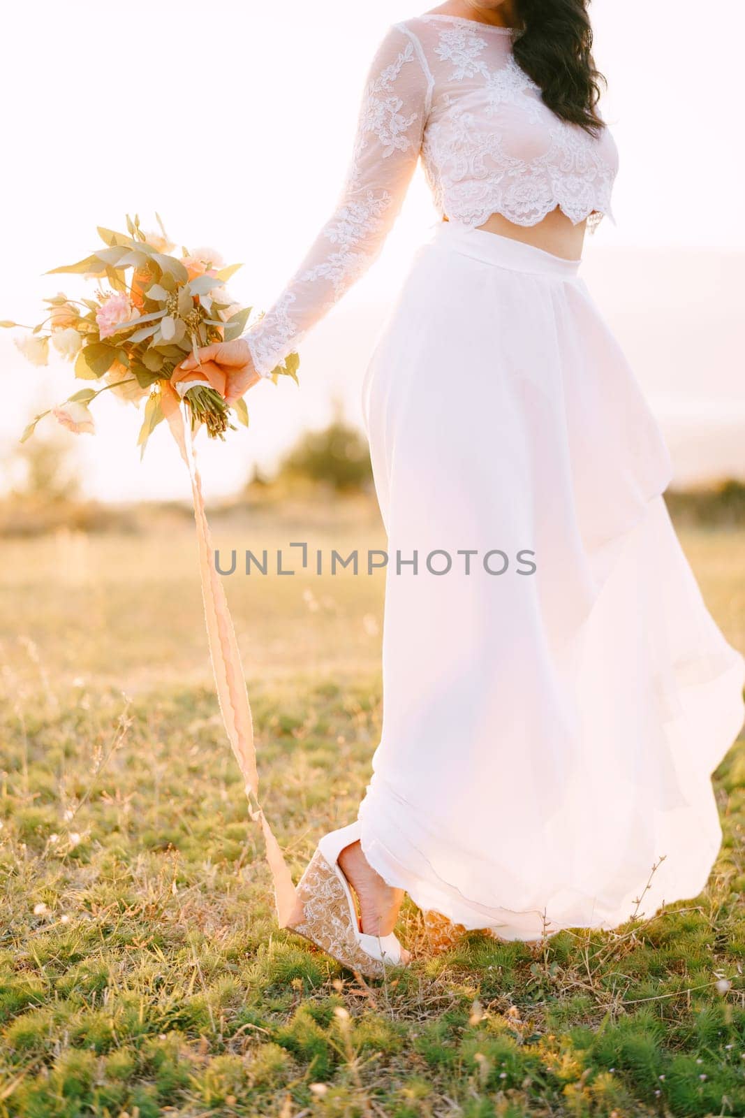 Bride with a bouquet stands on a green meadow with her hand to the side. Cropped. Faceless. High quality photo