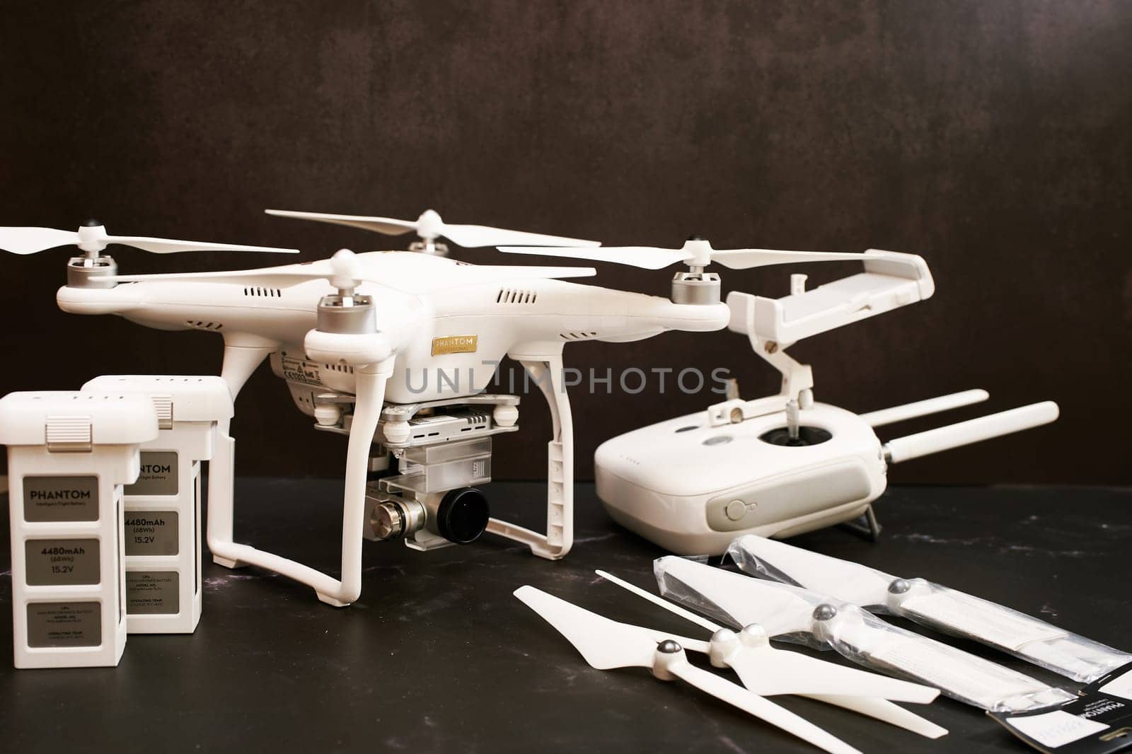 White DJI Phantom 3 UAV with spare batteries, propellers and control panel stands on a black table. High quality photo