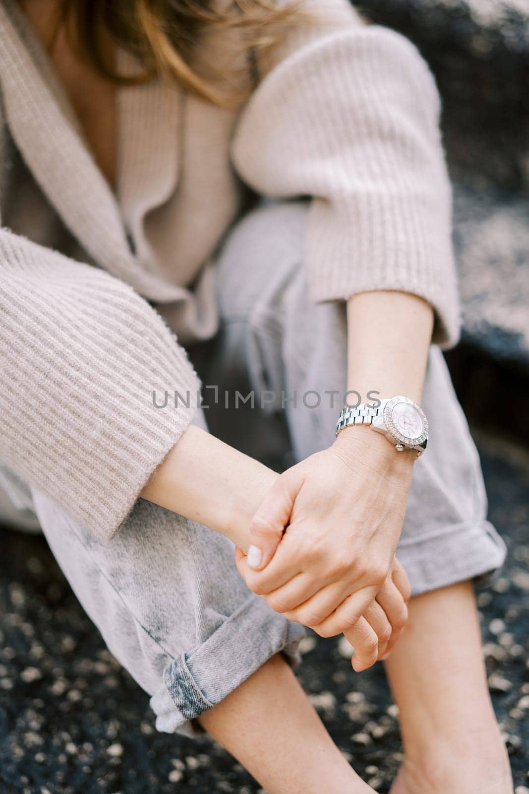 Girl in a sweater and jeans sits with her hands folded on her knees on stone steps. Cropped. Faceless. High quality photo