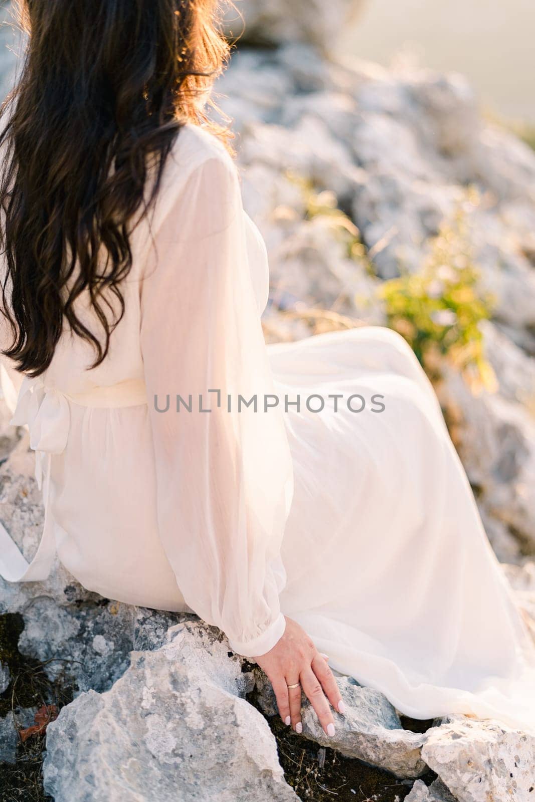 Bride sits on a rocky mountain in the sun. Side view. Cropped. High quality photo