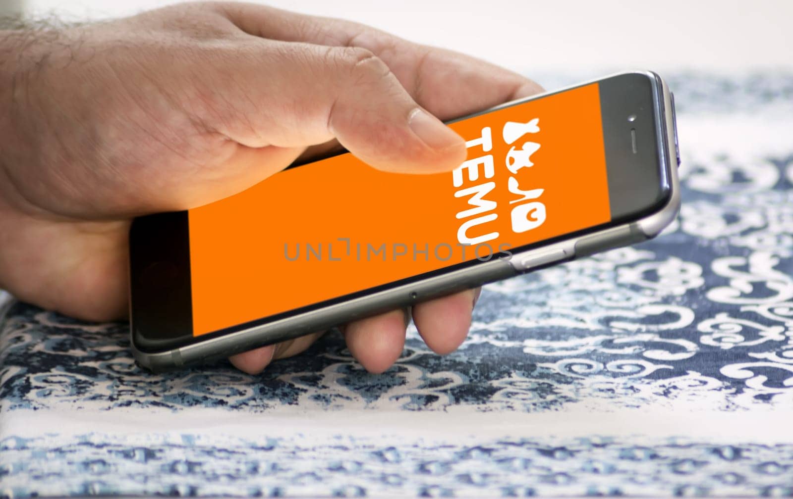 Boston, US, March 2023: Male hand holding a phone with Temu logo displayed on the screen. Blurred logo on the background. Temu is an online marketplace. Illustrative editorial