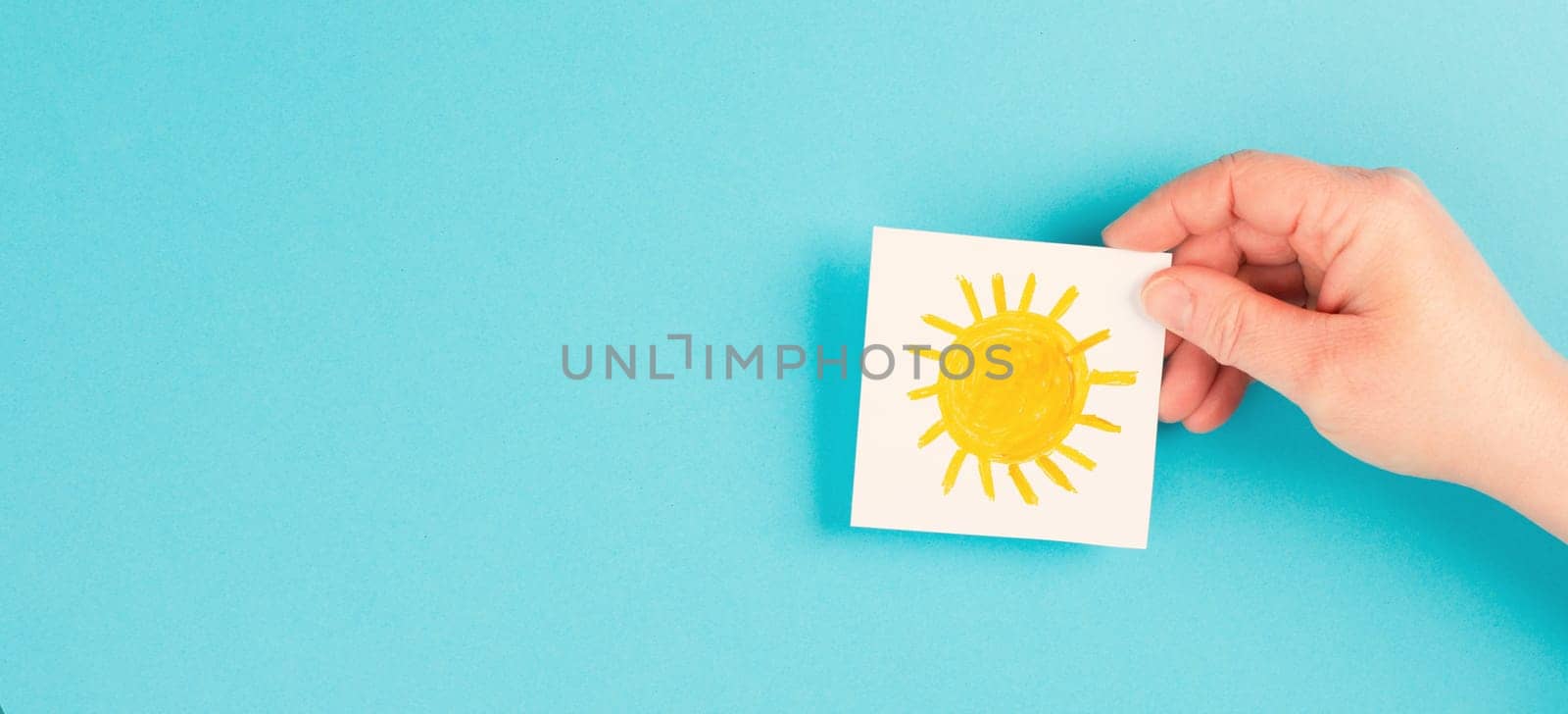 Holding a paper with a yellow sun, hot temperture on a summer day, positive attitude and hope, drawing of a child