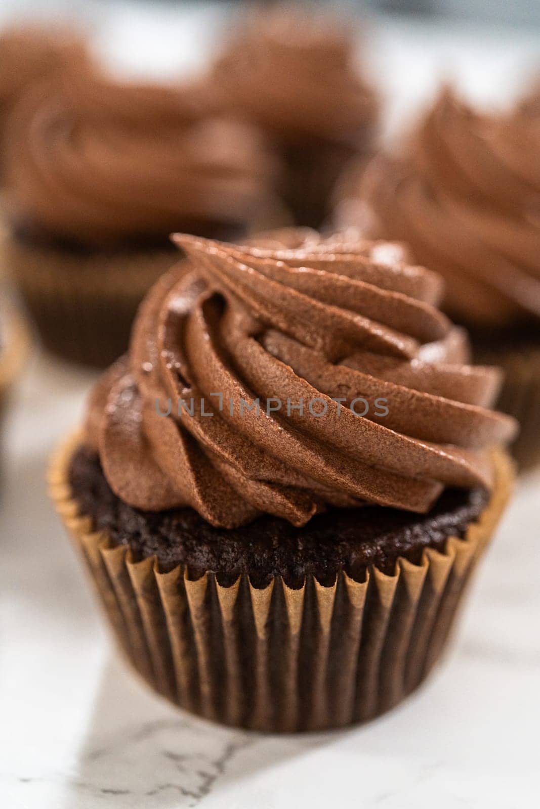 Delicate swirls of rich chocolate icing are meticulously piped onto each chocolate cupcake, creating an irresistible treat.