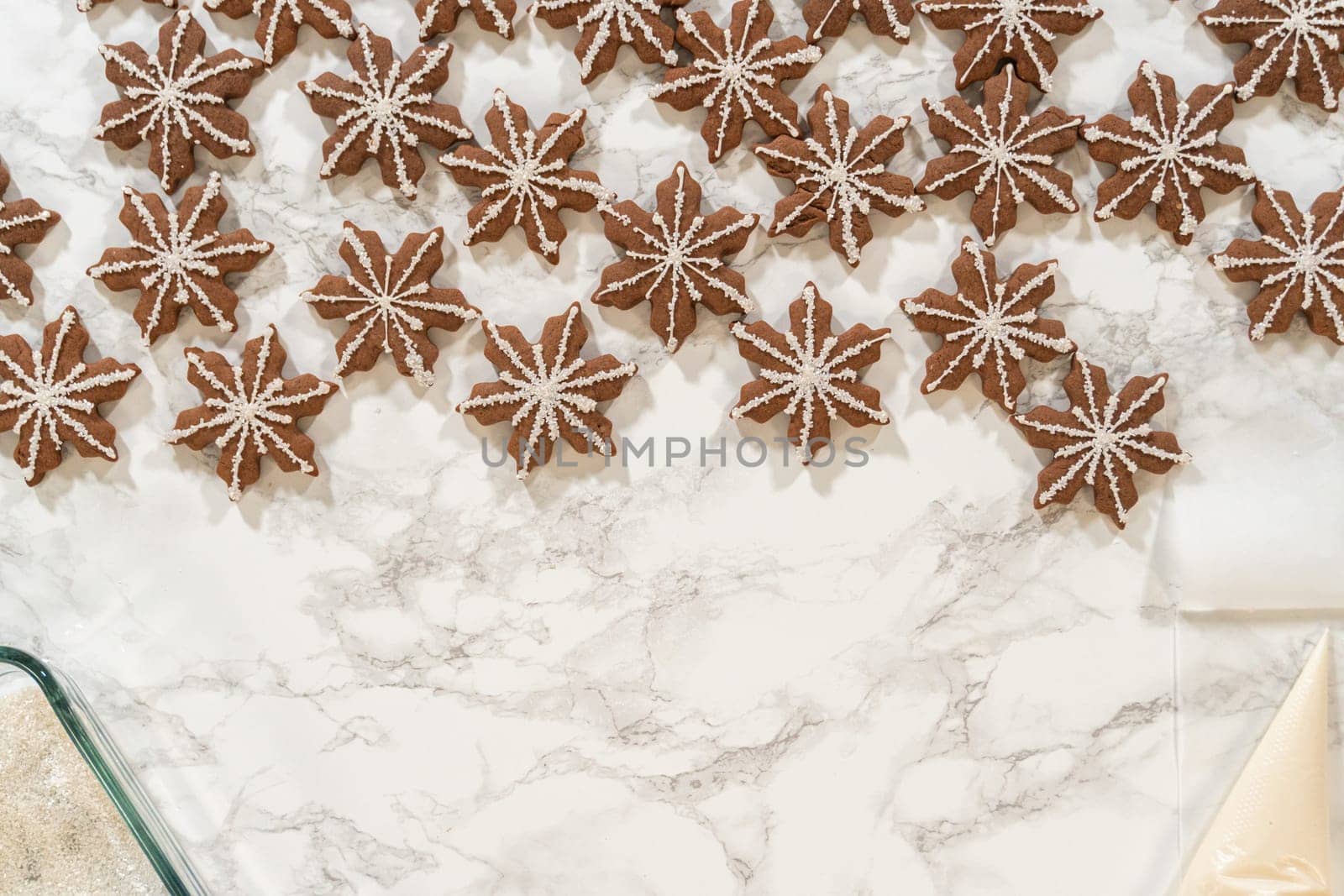 A wide shot of dozens of chocolate ginger snowflake cookies, some decorated with royal icing and sugar crystals, laid out neatly on a marble surface in a festive arrangement