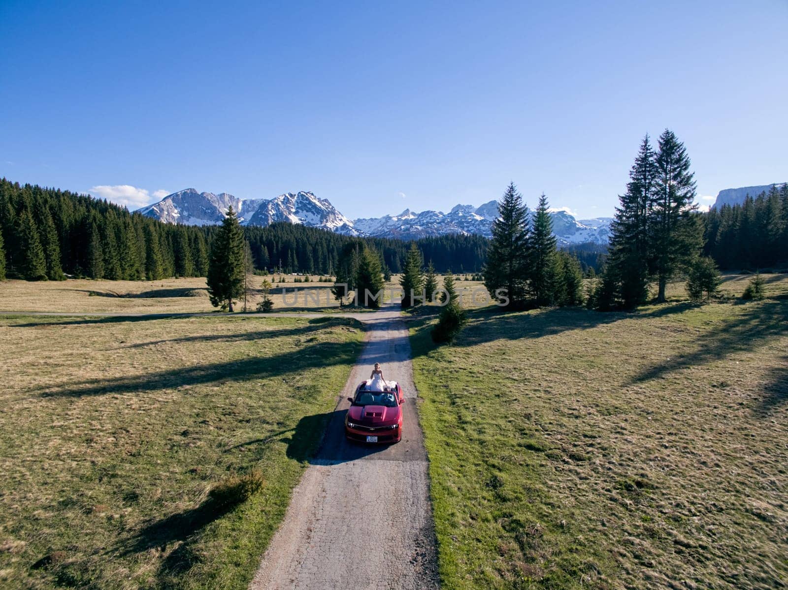 Bride and groom are riding in a cabriolet along a highway in a mountain valley. Drone. High quality photo