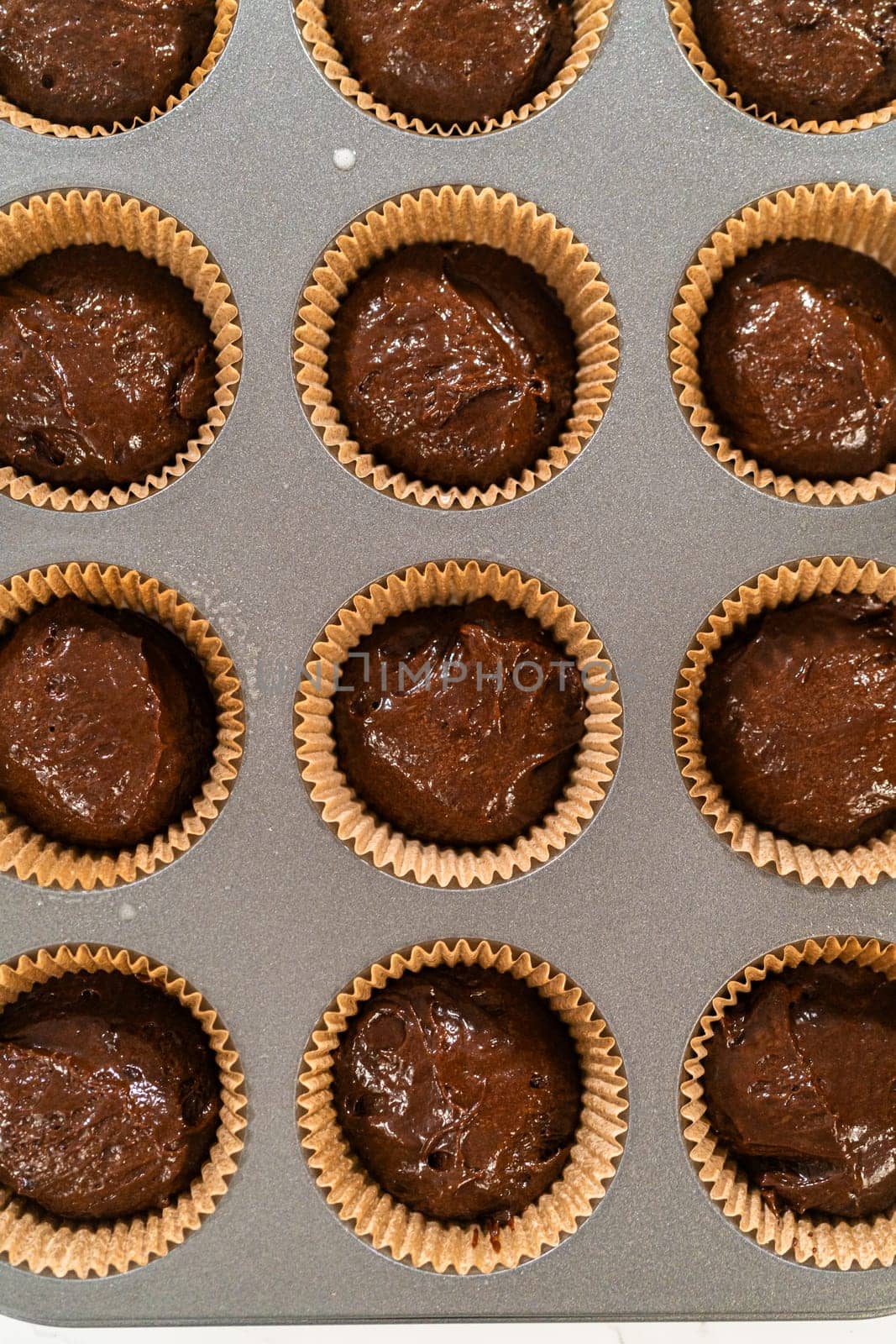 The process involves carefully scooping the rich batter into the waiting cupcake pan.