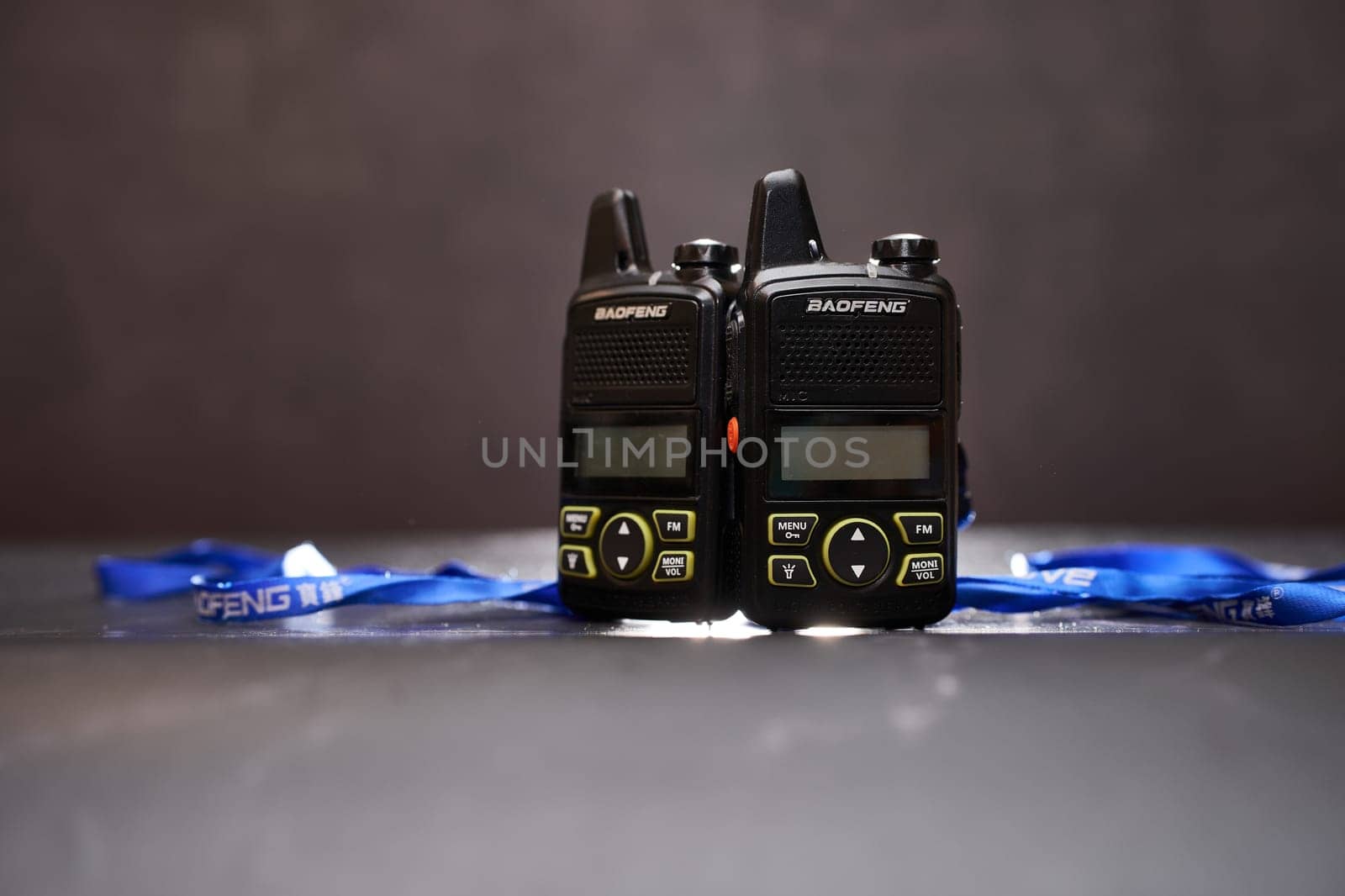 Two black Baofeng BF-T1 walkie-talkies with blue ribbons stand on a black table. High quality photo