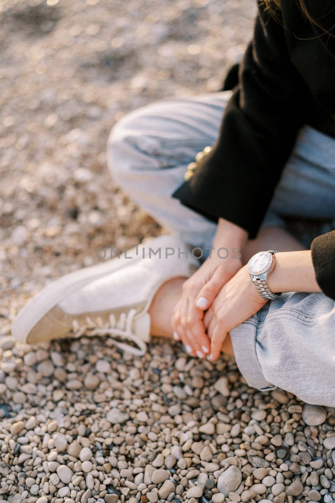 Girl sits with her hands crossed on her leg on a pebble beach. Cropped. Faceless. High quality photo