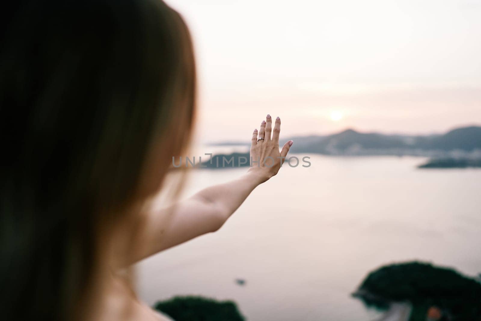 Girl examines her hand with a wedding ring against the background of the sky over the sea. Back view. High quality photo
