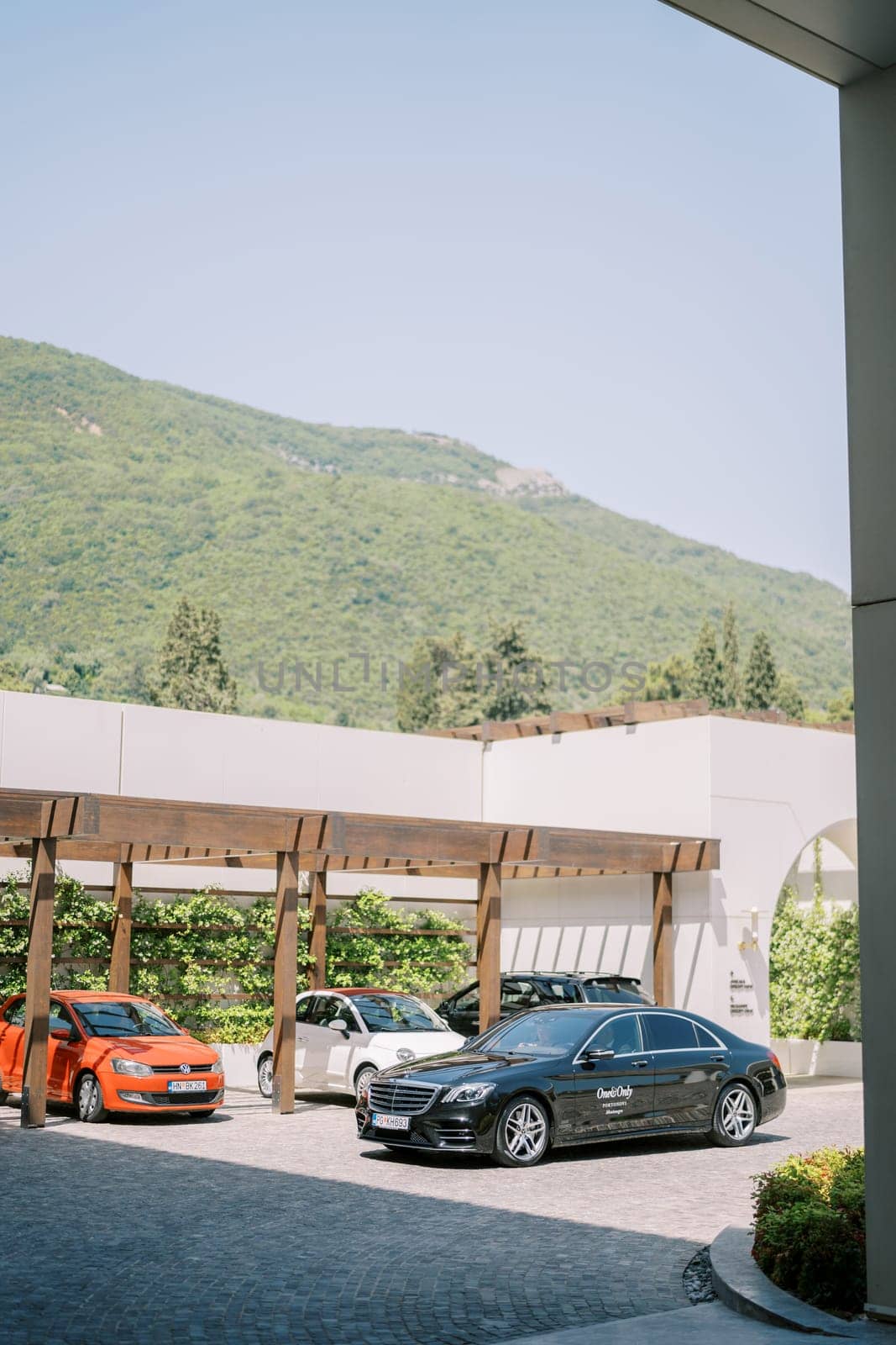 Multi-colored cars stand in the hotel parking lot under a wooden canopy at the foot of the green mountains. High quality photo