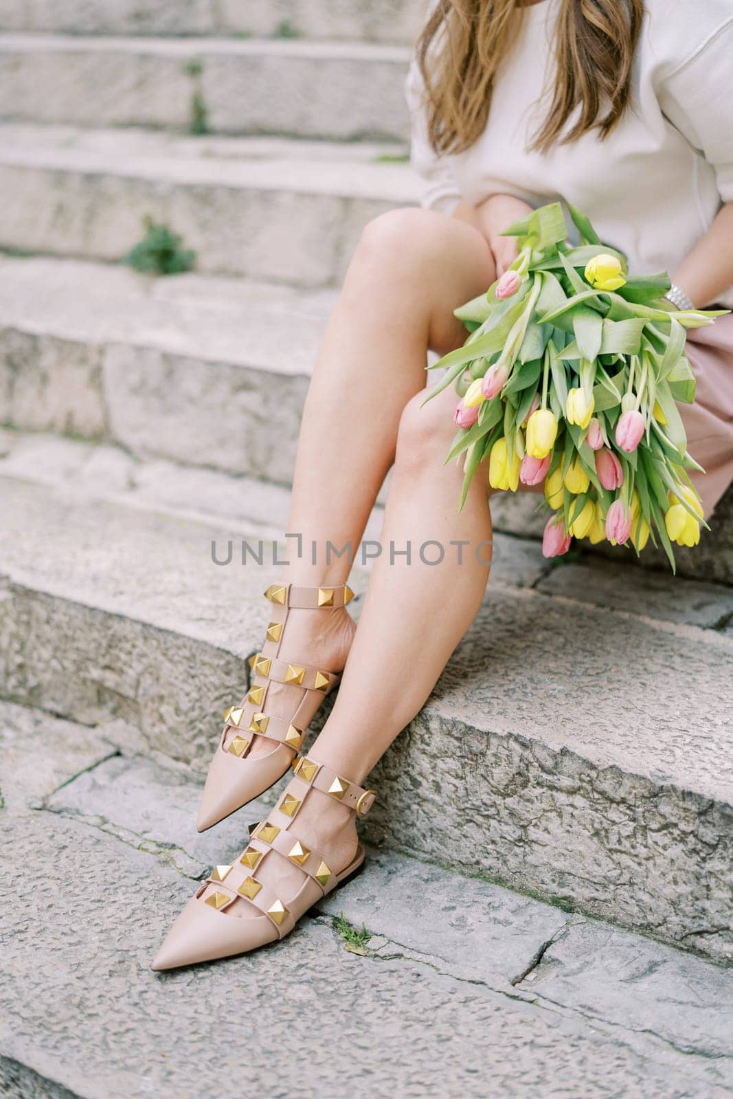 Girl sits on stone steps with a colorful bouquet of flowers. Cropped. Faceless. High quality photo