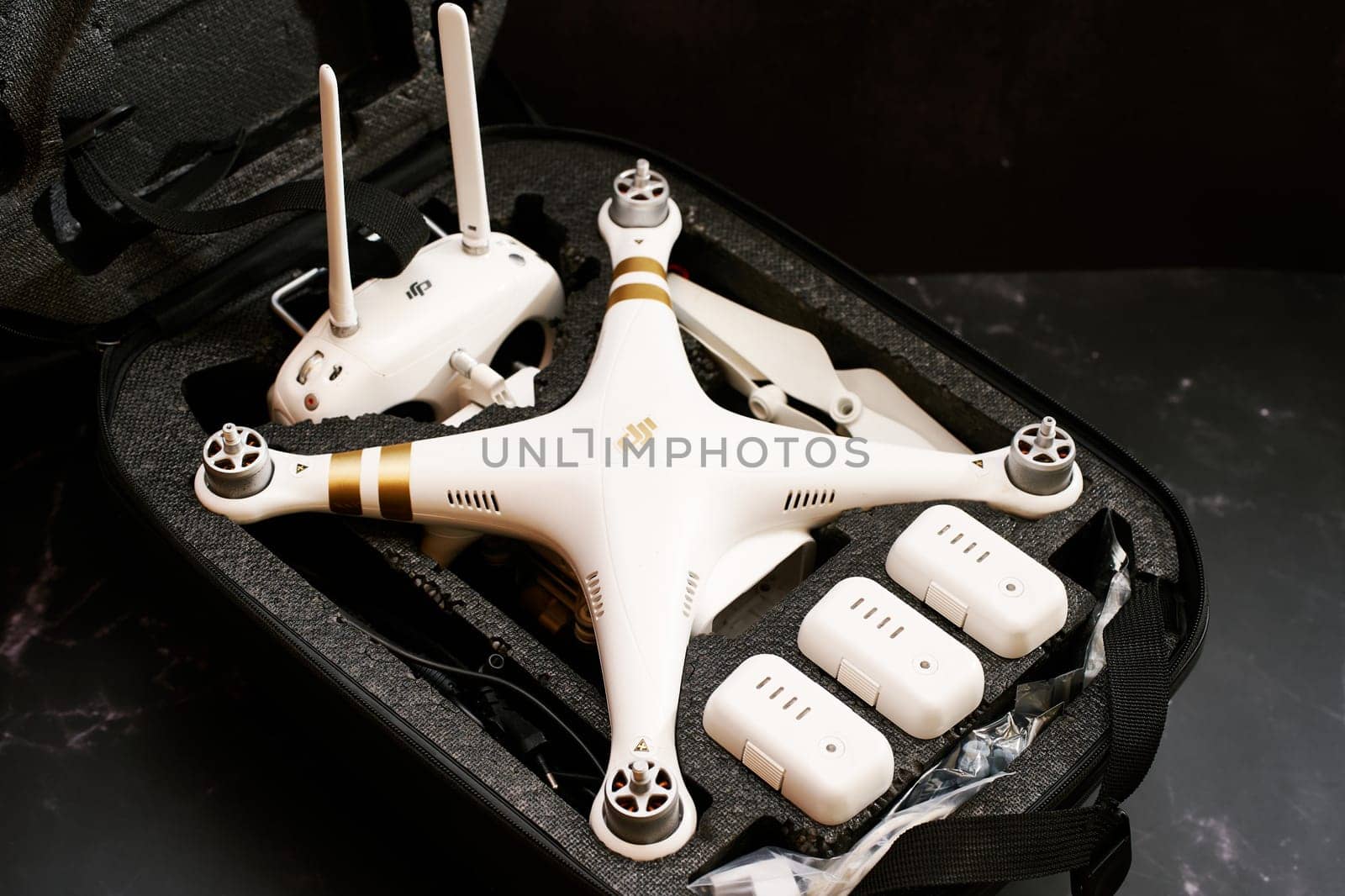 White DJI Phantom 3 drone with spare batteries and a control panel lies in a protective case on a black table. High quality photo