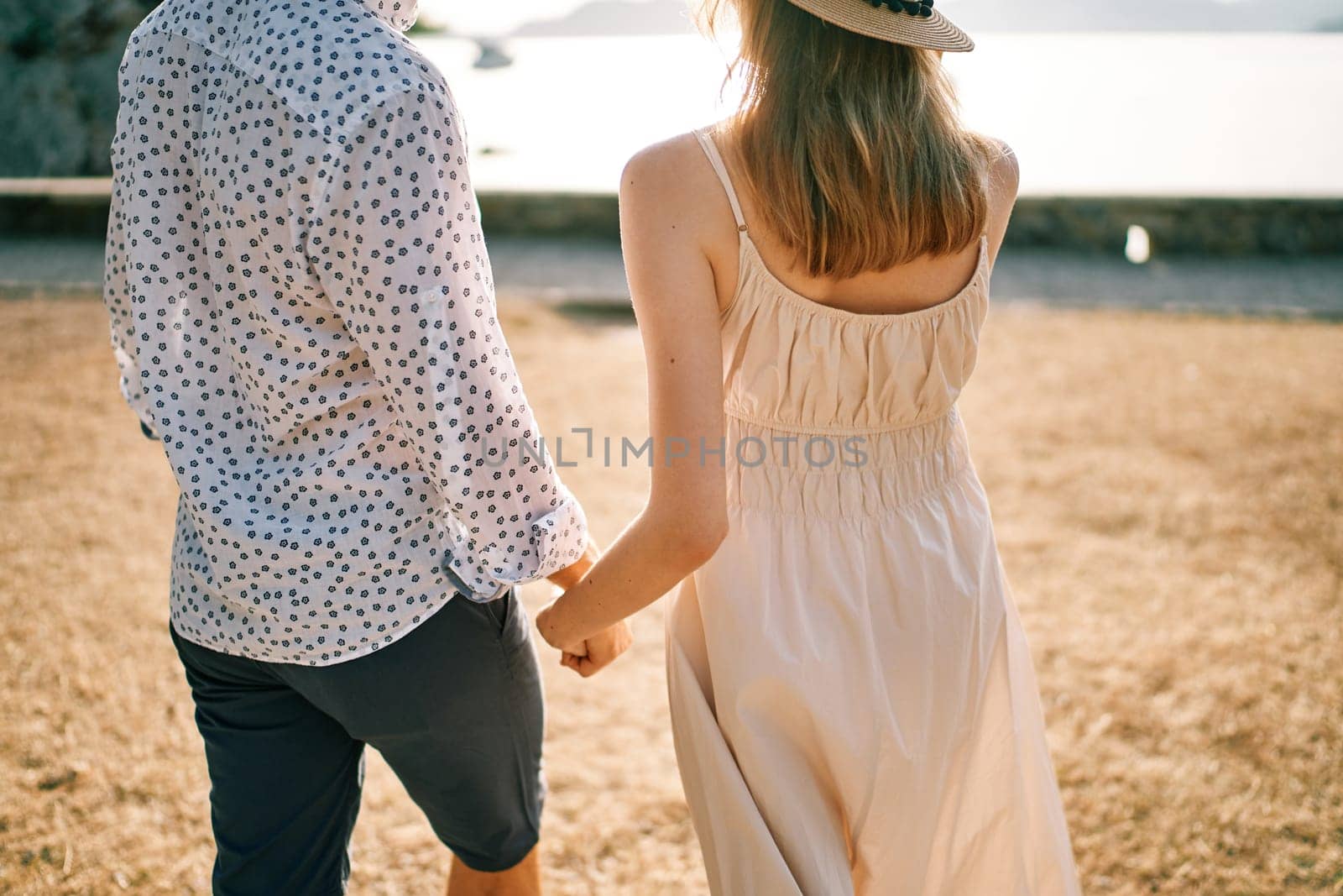 Man and woman walk along the seashore holding hands. Back view. Cropped. High quality photo