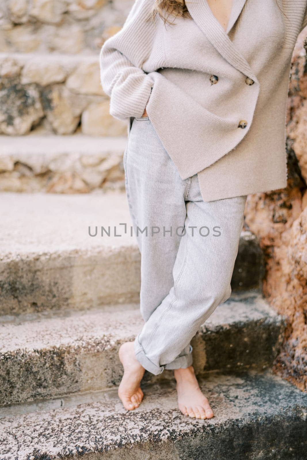 Barefoot young woman stands on the stone steps, crossing her legs and leaning on the wall. Cropped. Faceless. High quality illustration