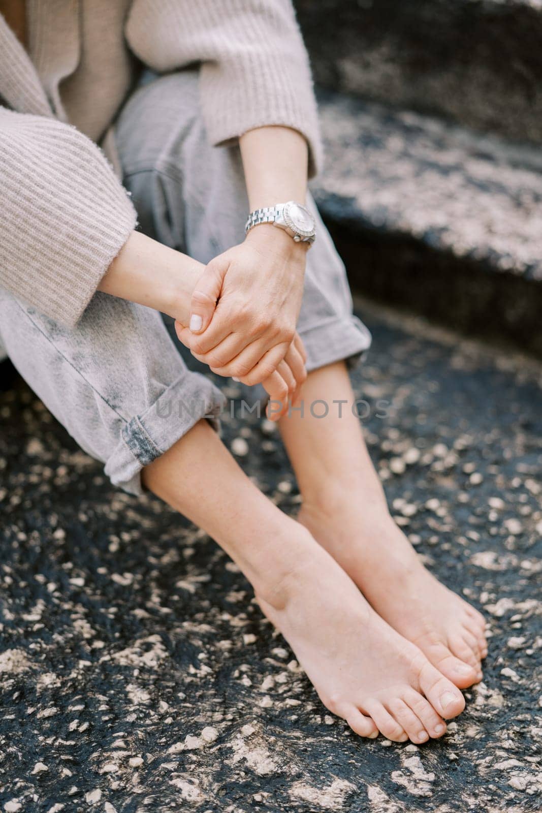 Barefoot girl sits with her hands folded in her lap on the stone steps. Cropped. Faceless. High quality photo