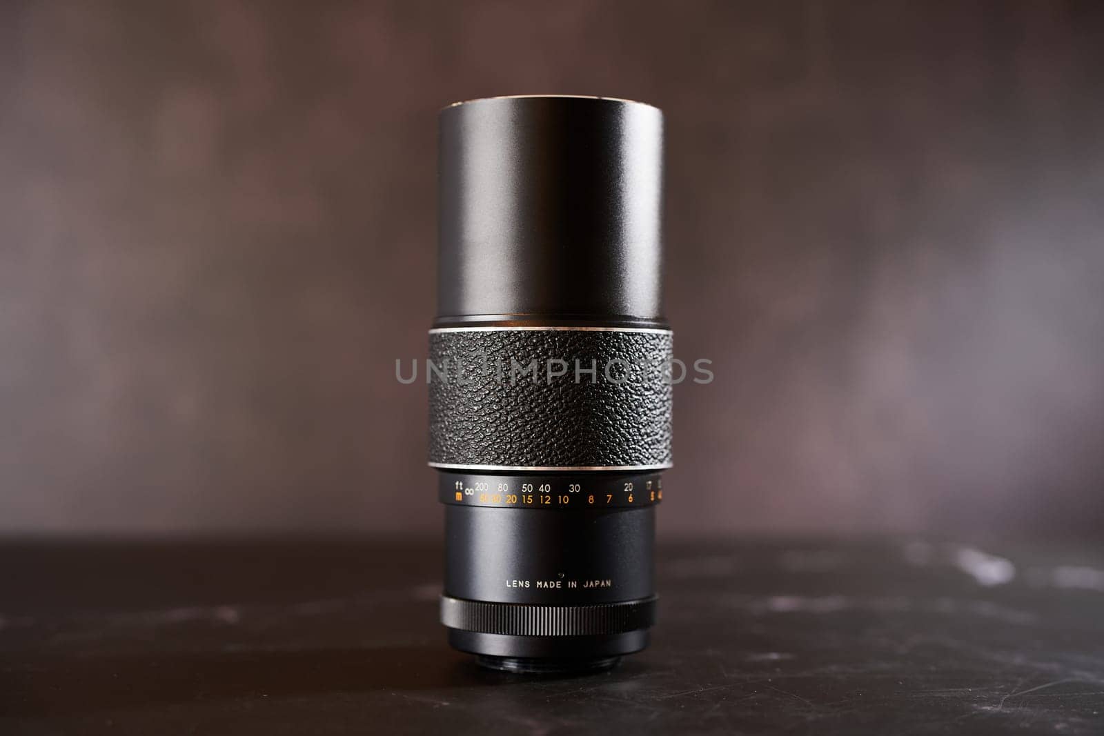 Vintage Chinon M42 telephoto lens stands on a black table. Caption: Lens made in Japan. High quality photo