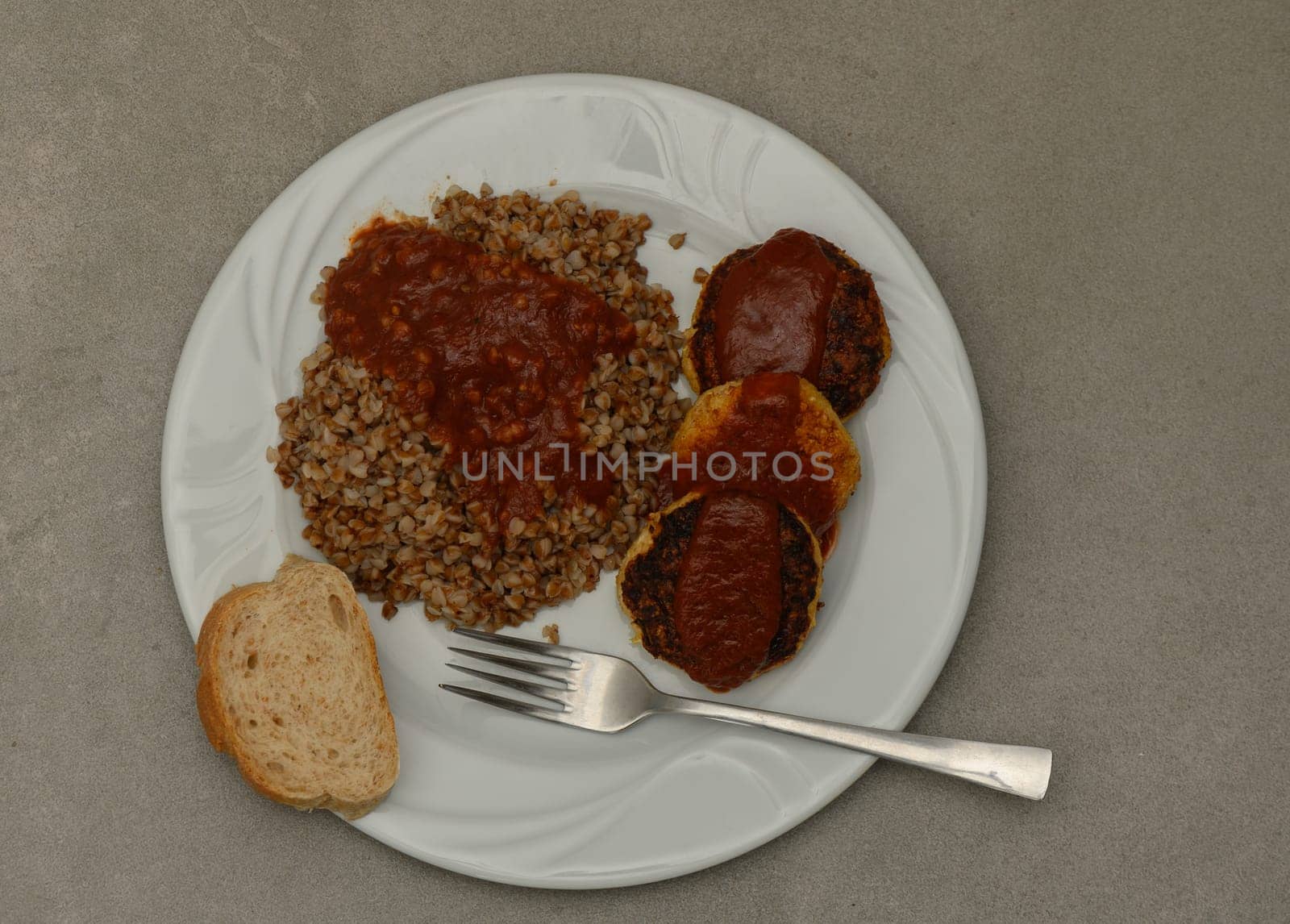 Savor the comforting flavors of bulgur wheat paired with succulent meat patties generously drizzled with rich sauce, all set on a simple white plate. A slice of bread completes the meal.