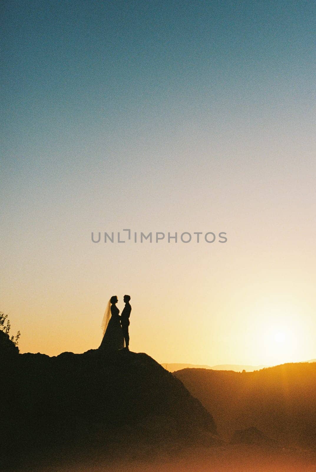Bride and groom stand on the mountain holding hands opposite each other at sunset. High quality photo