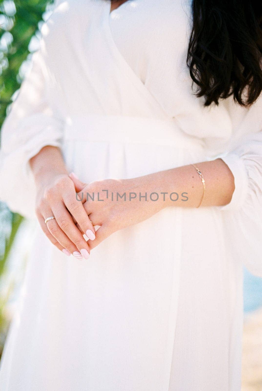 Bride folded her hands in front of her standing by the sea. Cropped. Faceless. High quality photo