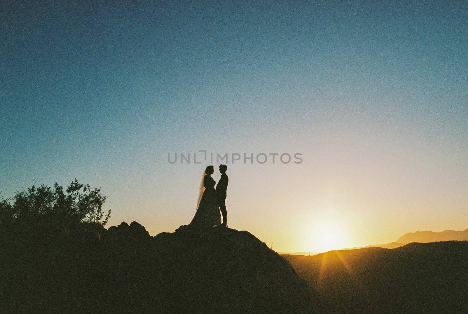 Bride and groom stand on the mountain holding hands at sunset. High quality photo