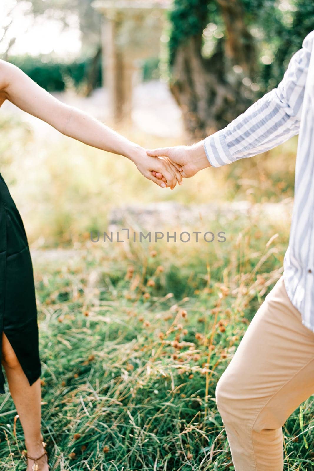 Man follows woman through the park, holding her hand. Cropped. Faceless. High quality photo