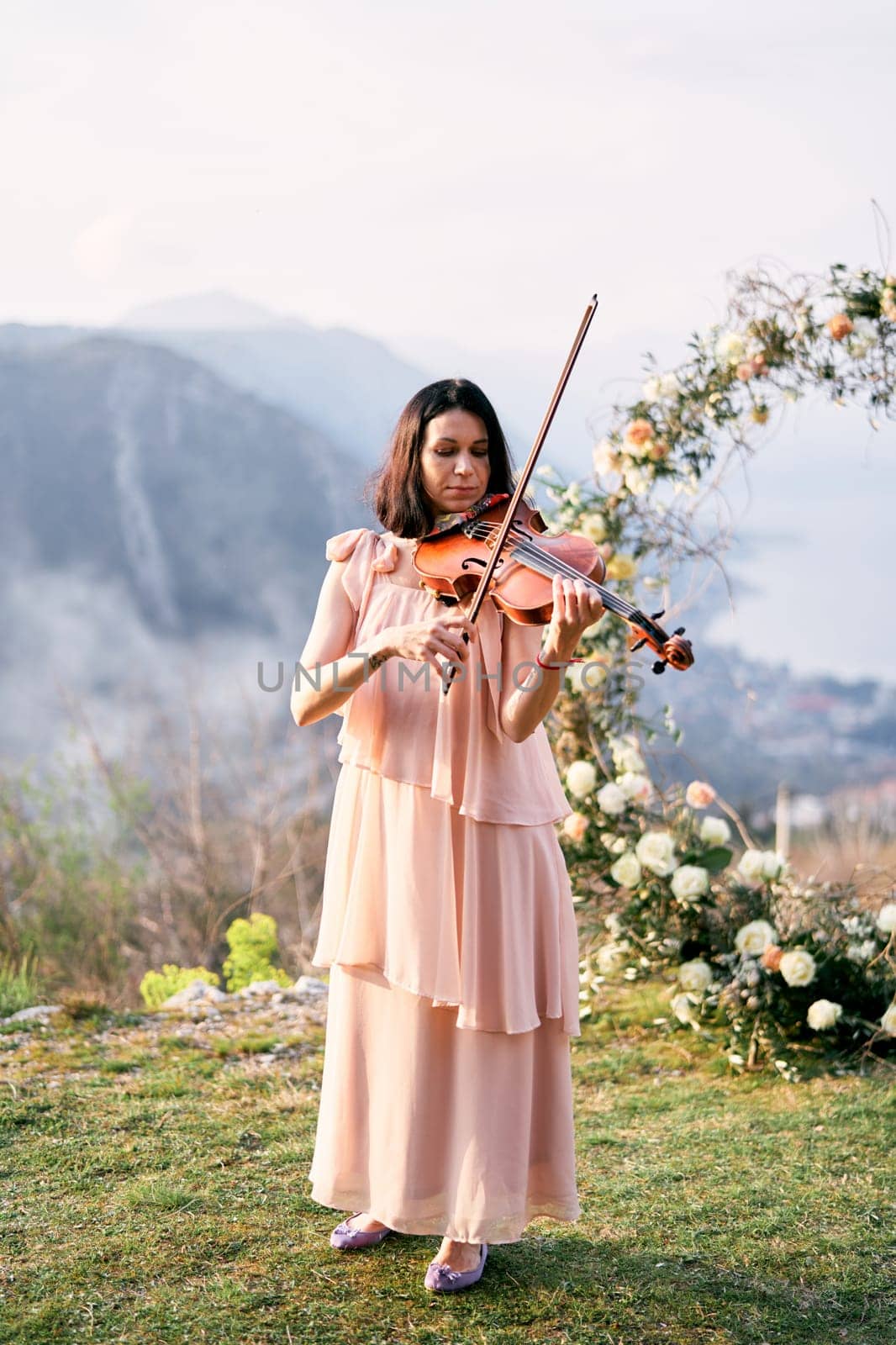 Girl musician plays the violin near the wedding arch on the mountain. High quality photo