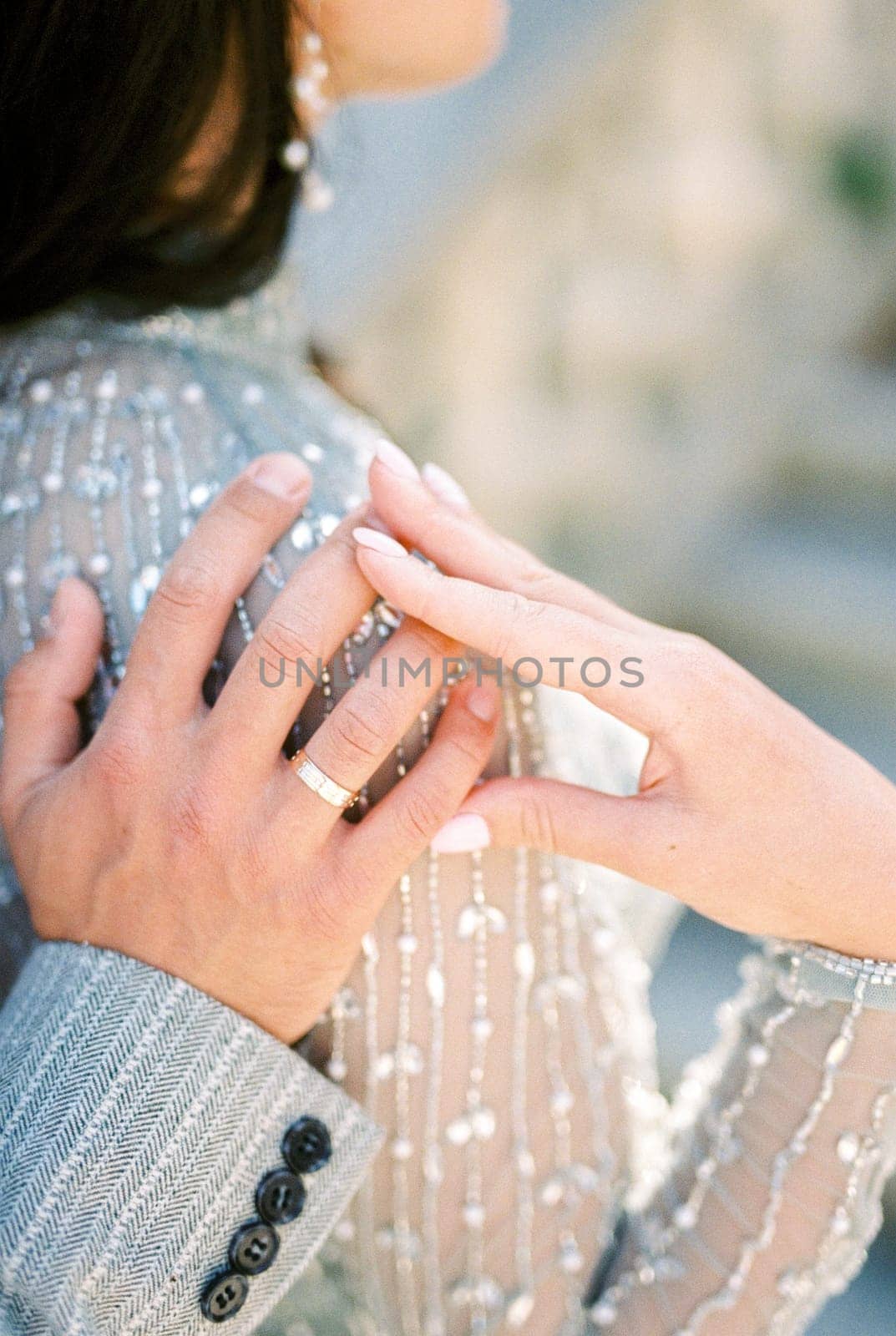 Bride put her hand on the hand of groom hugging her shoulder. Back view. Cropped. High quality photo