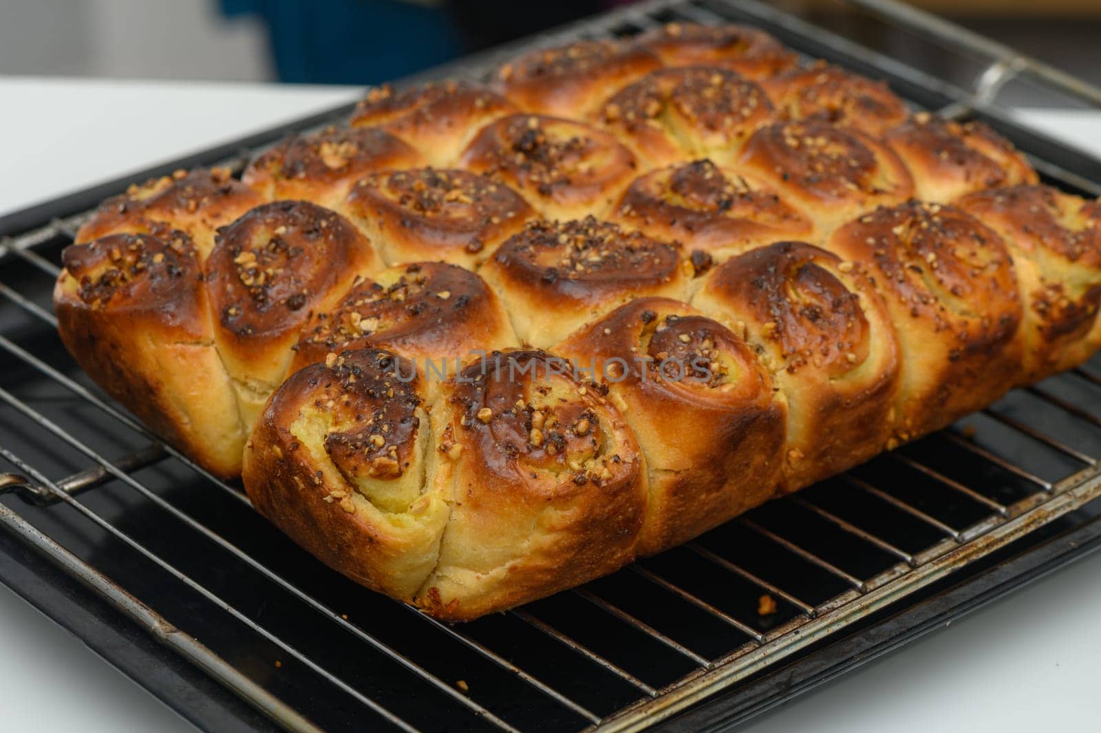 Sweetly spiced cinnamon rolls emerging from the oven, boasting a golden crust and sprinkled with crunchy nuts, create a delightful aroma in a warm kitchen atmosphere.