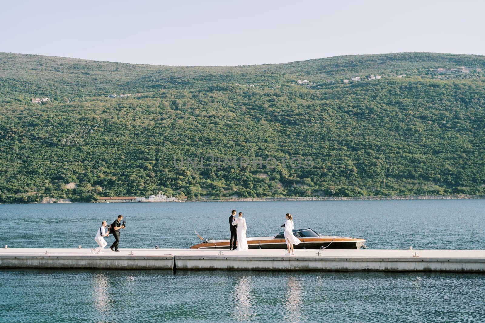 Photographers take pictures of bride and groom standing on the pier near a motor boat. High quality photo