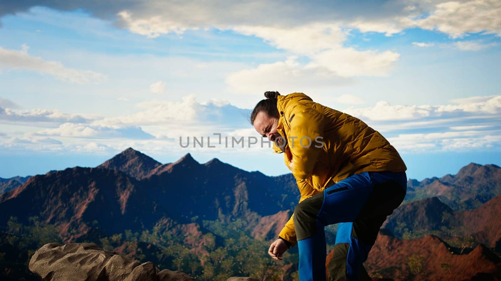 Reckless unprepared hiker stumbles near the edge of a high altitude cliff, caught off guard by strong winds. Unequipped for the extreme conditions, losing balance on mountain top. Camera A.