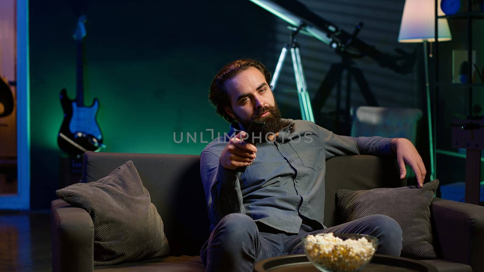 Man using remote to switch channels on television screen, feeling frustrated by uninteresting content. Bored person scrolling through TV channels, upset after not finding anything watchable, camera A