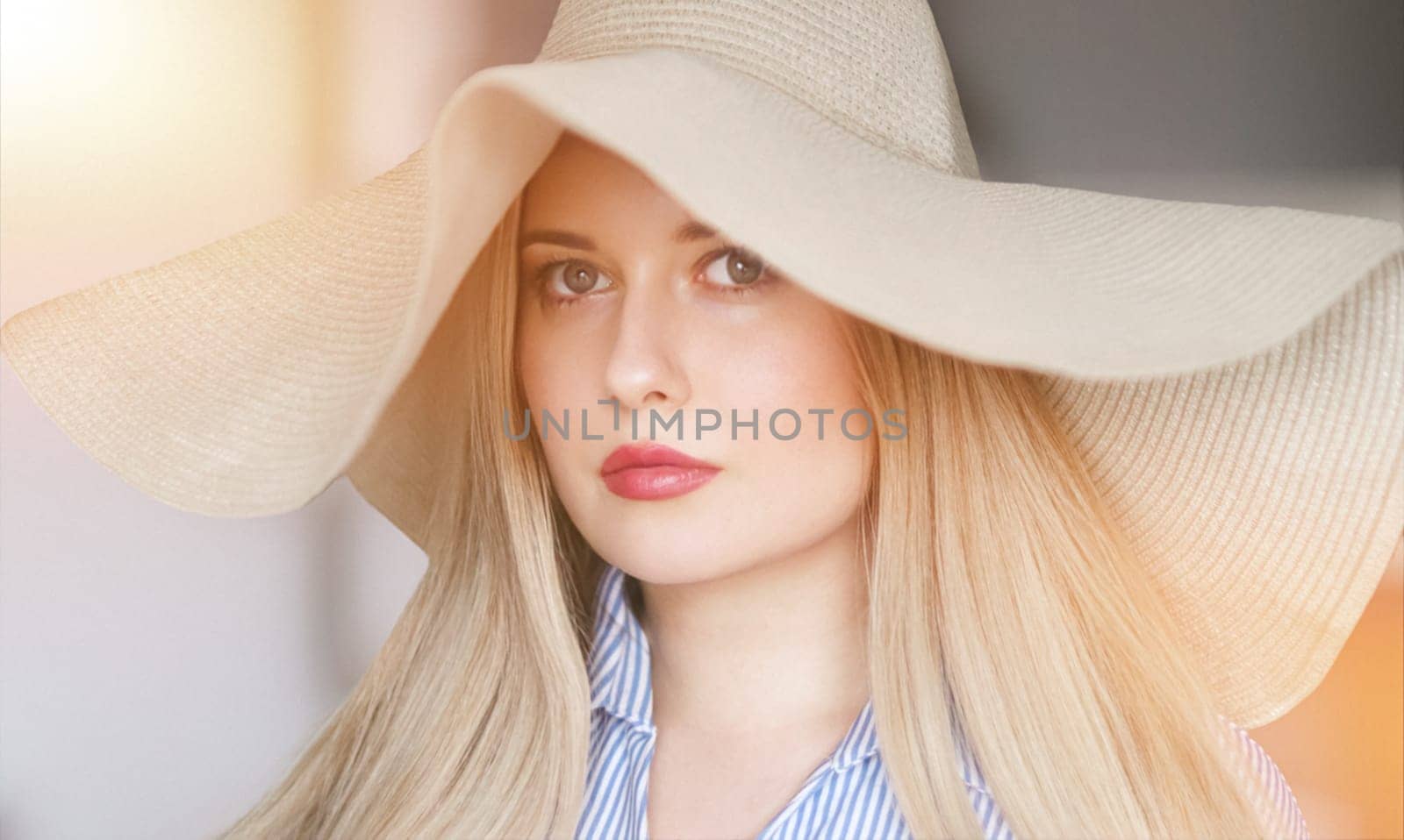 Woman, fashion and summer country charm, blonde beauty and elegance in wide brimmed beach hat. Feminine allure, timeless style and graceful glow. Smile, straw hat and blue striped blouse, natural lighting and effortless charm, fashion look idea