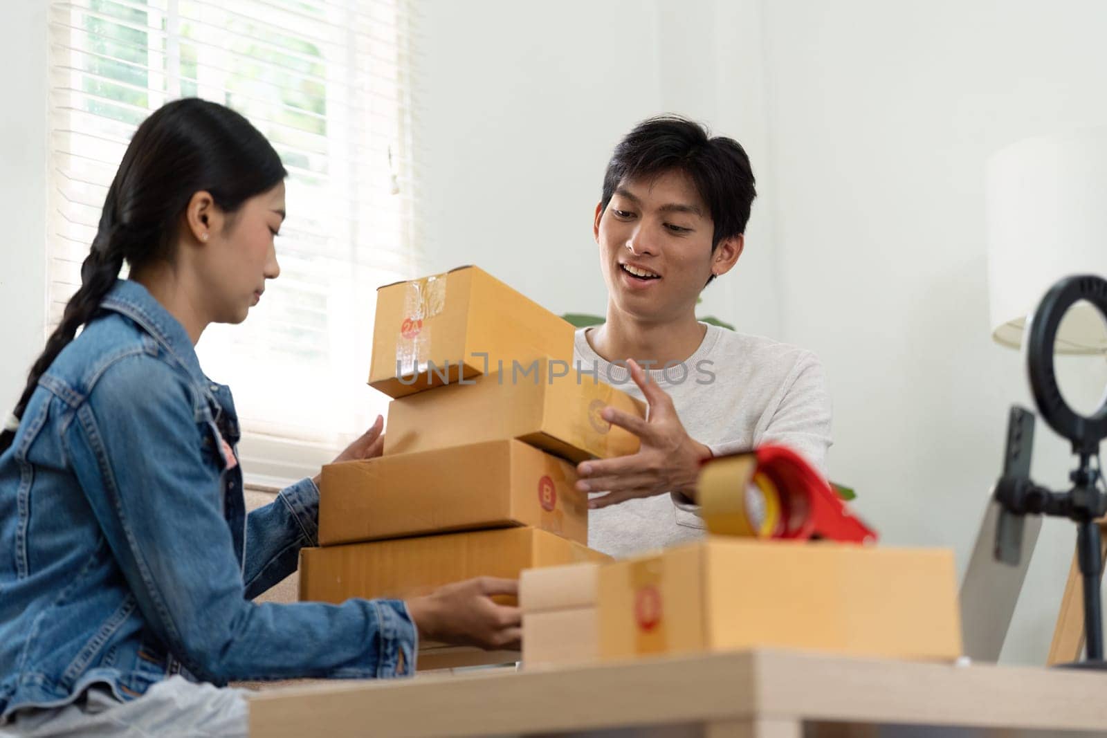 An entrepreneurial couple collaborates in their living room, packing boxes and preparing their shipment deliveries, displaying teamwork and dedication to their business.