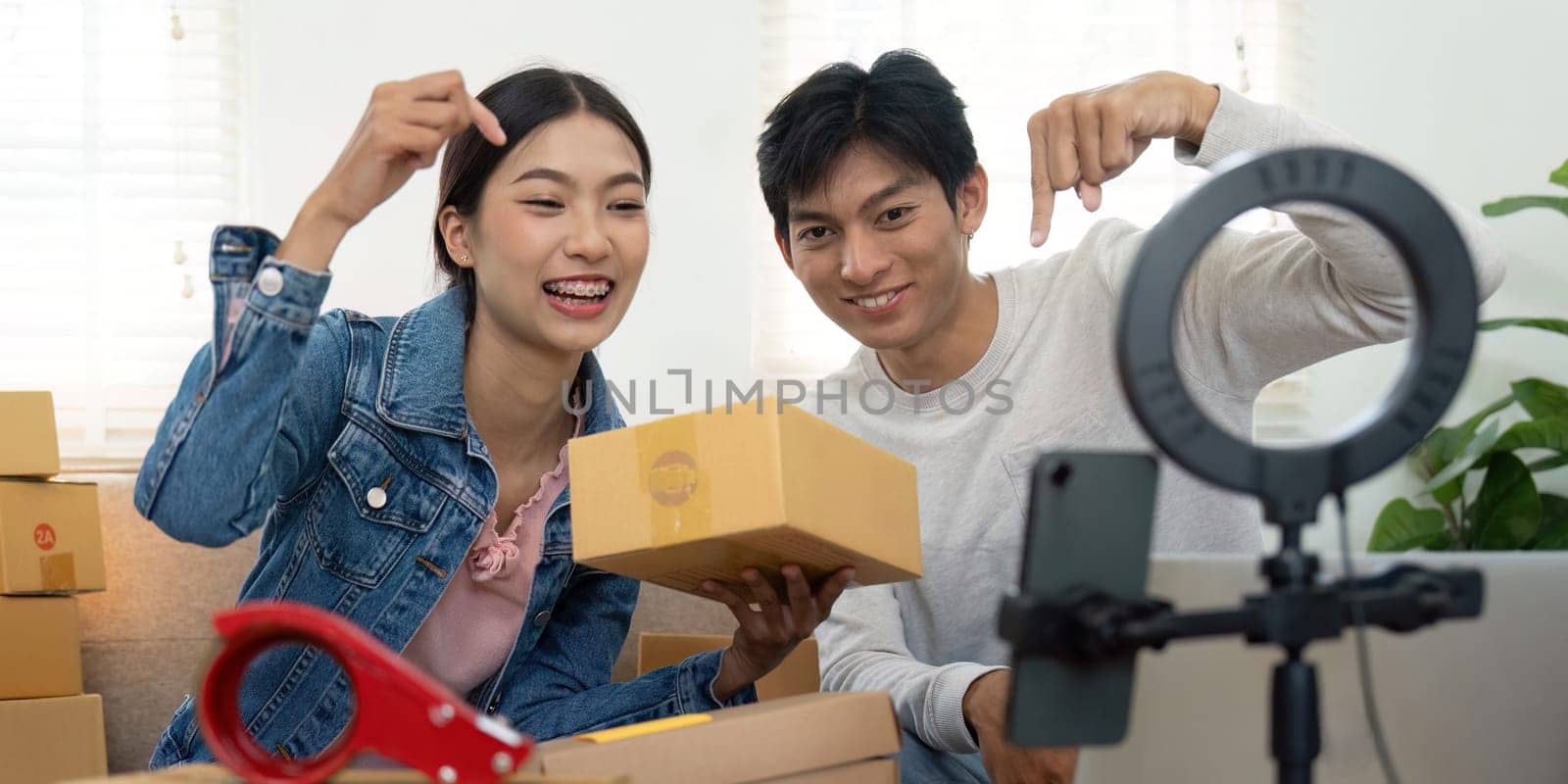 The happy couple holds up a package while filming a video for their audience, highlighting their enthusiasm for their products as they work together in their creative business venture.