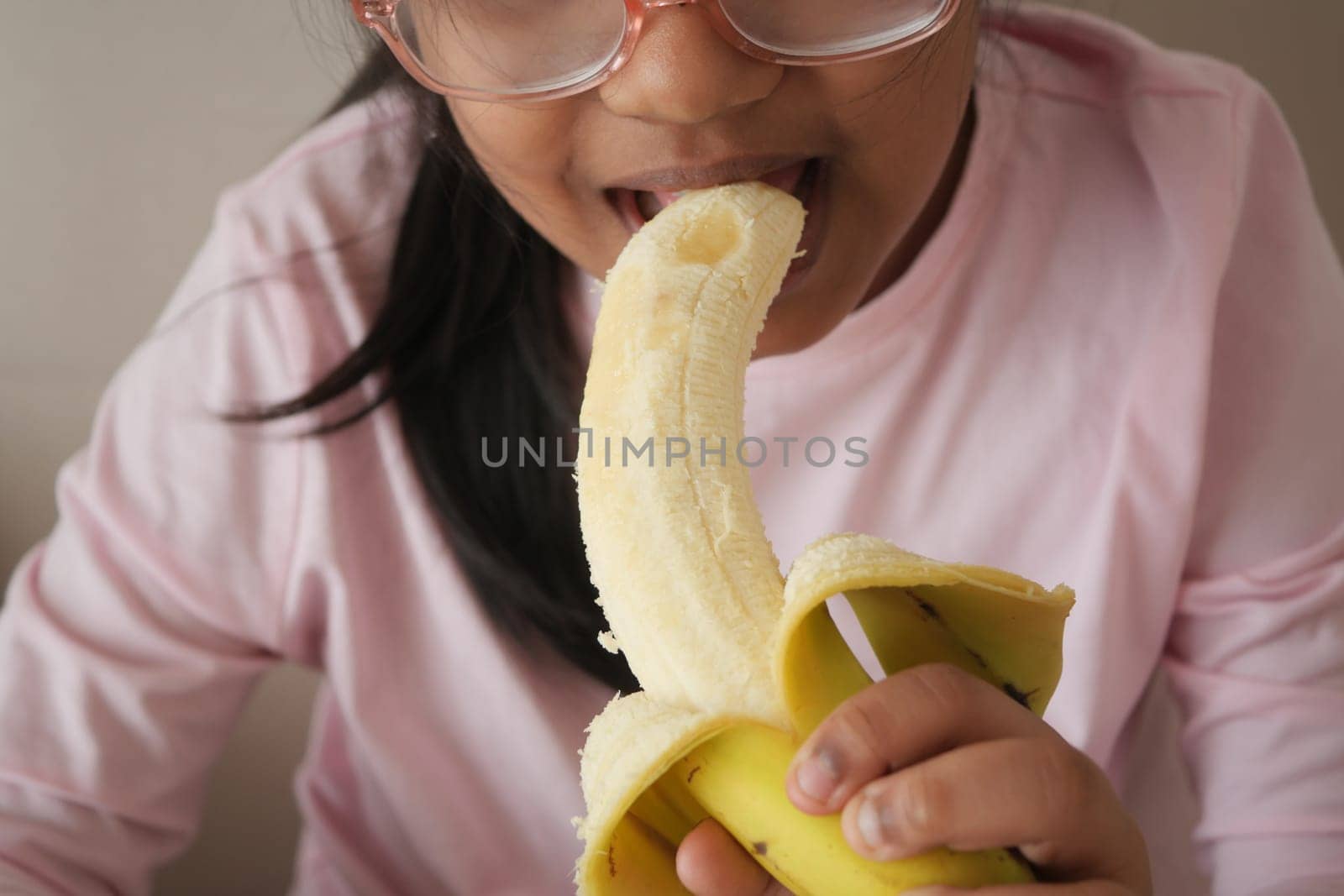A child bites into a ripe banana while sitting indoors.