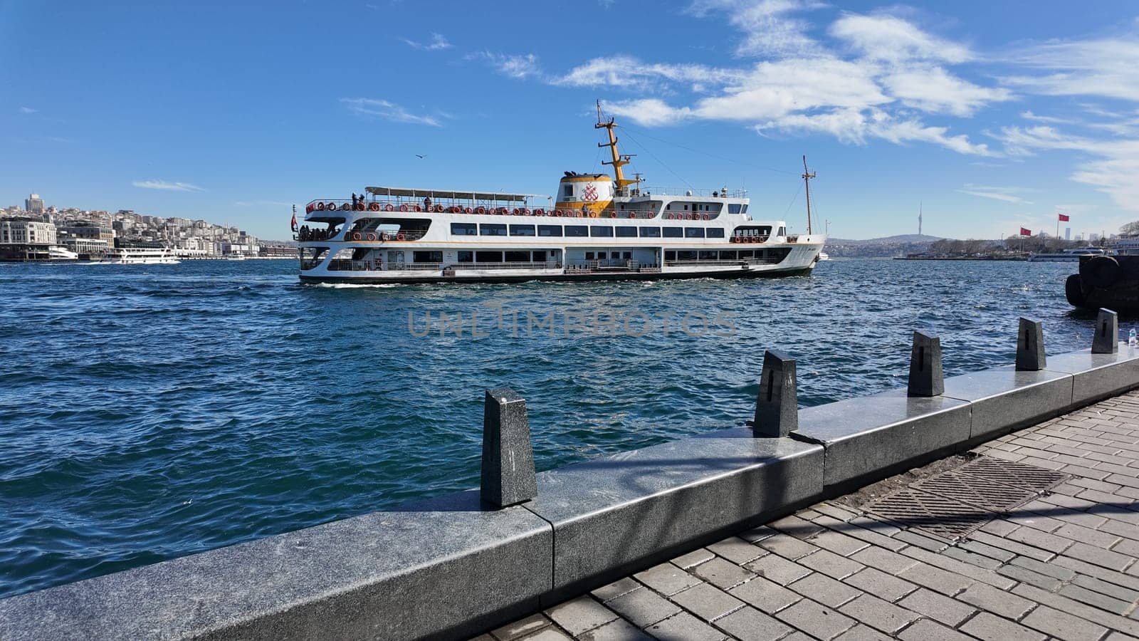 A ferry sails across the vibrant waters with a city backdrop under blue skies.