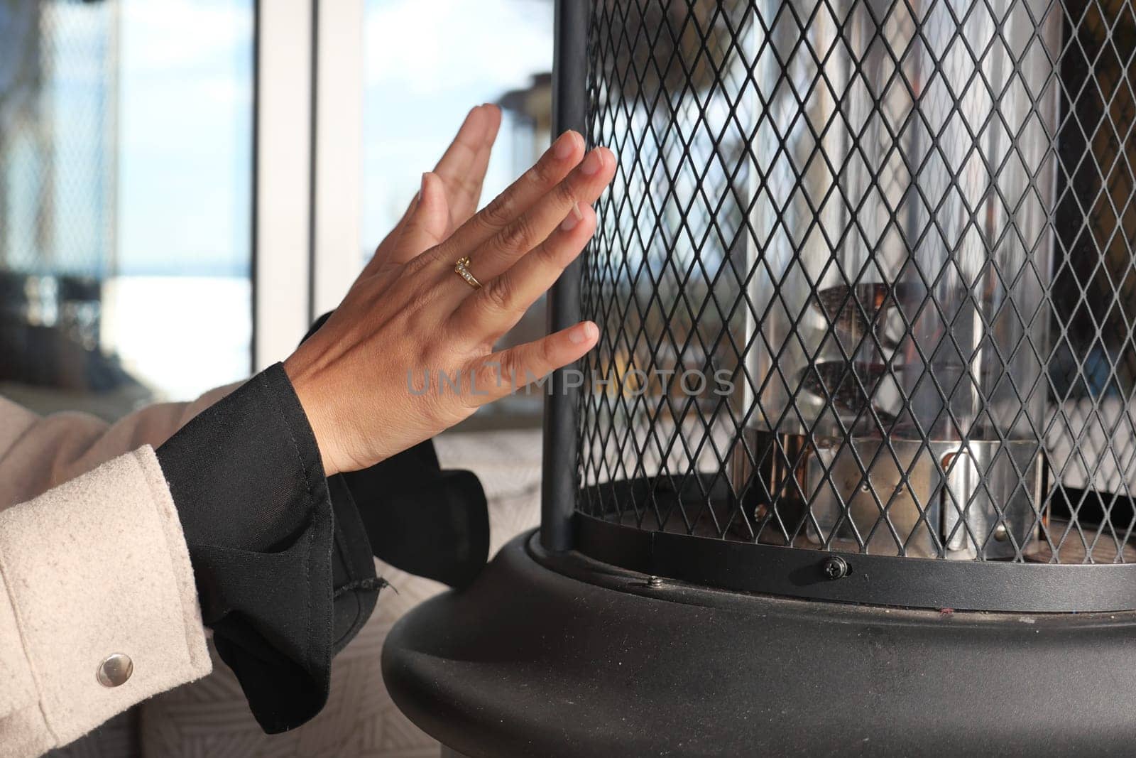 A hand reaches towards a heater for warmth in a cozy indoor setting.