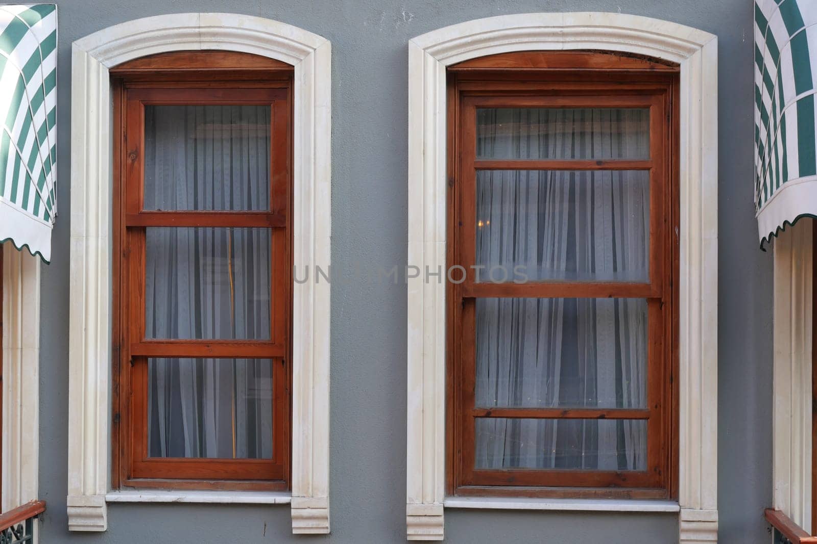 Two wooden windows with sheer white curtains framed in a gray wall.
