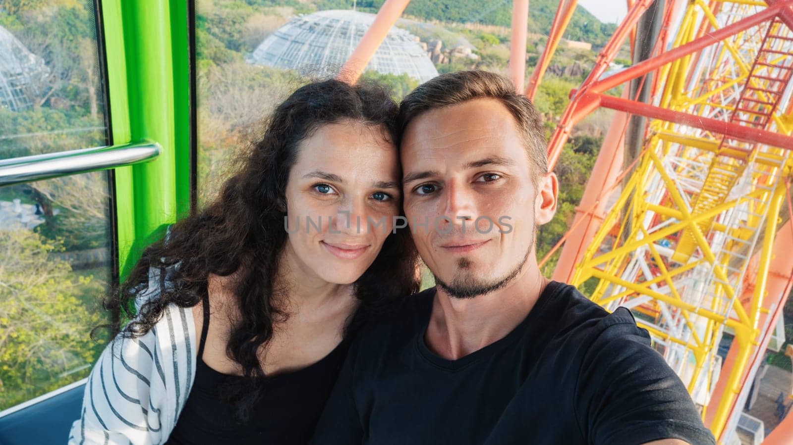 Selfie of happy couple tourists travelers in love in cabin of a ferris wheel in amusement park on summer vacation