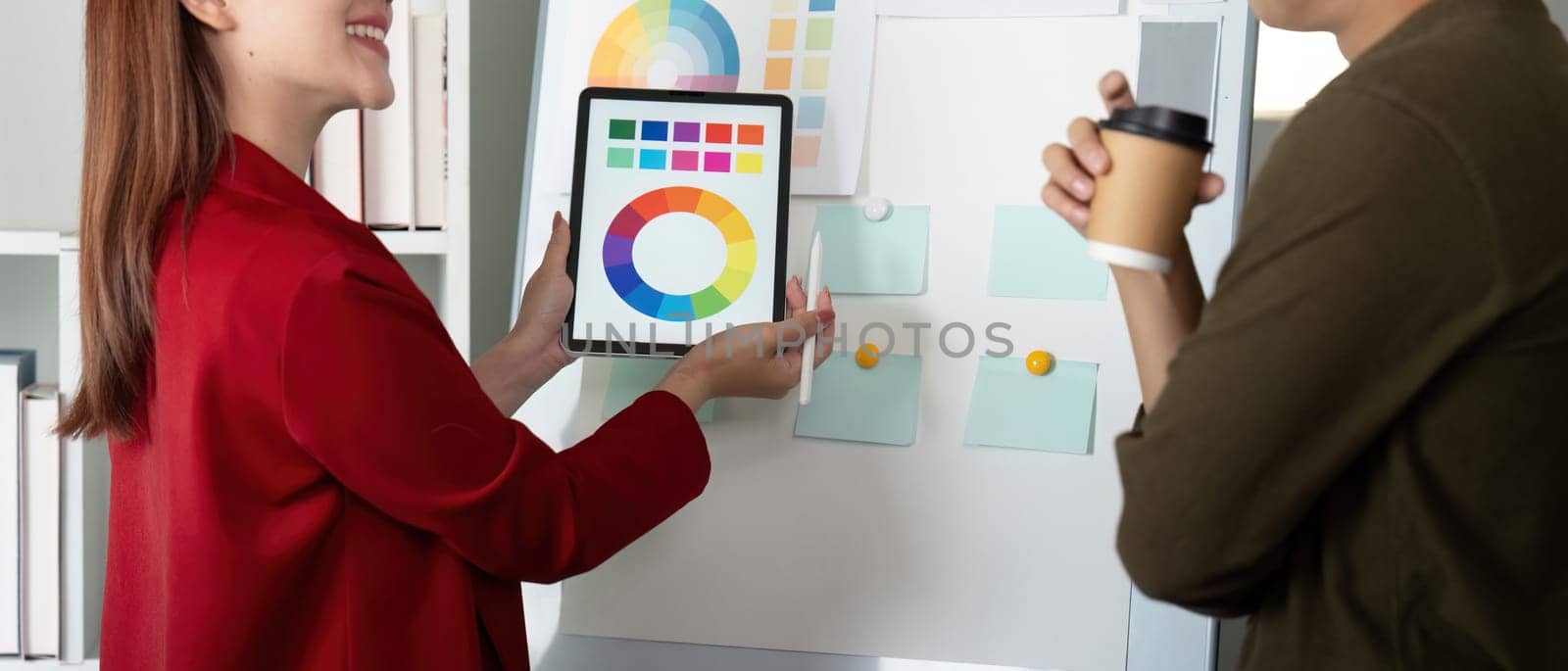 In a vibrant workspace, a designer engages with a colleague, showcasing color palettes on a tablet, fostering collaboration and creativity.