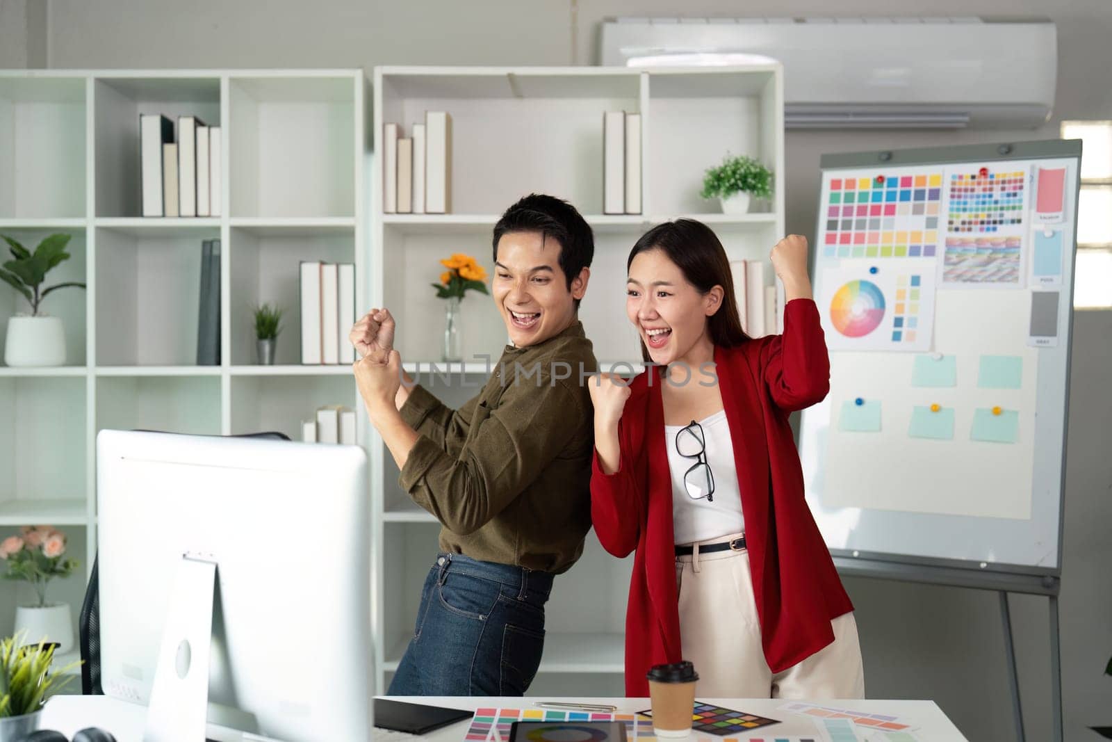 With excitement, the two designers express their happiness over a successful project outcome, showcasing teamwork in a lively office environment.