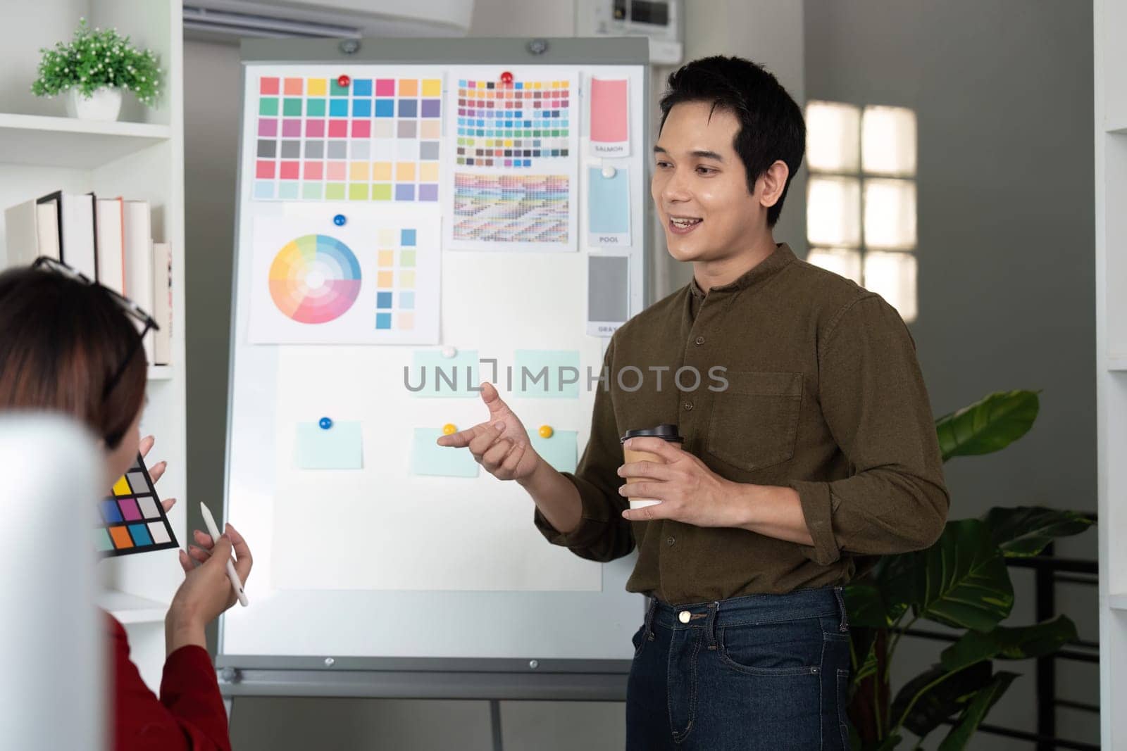 During a brainstorming session, a male designer enthusiastically gestures to his colorful presentation, engaging a seated colleague in meaningful design discussions.