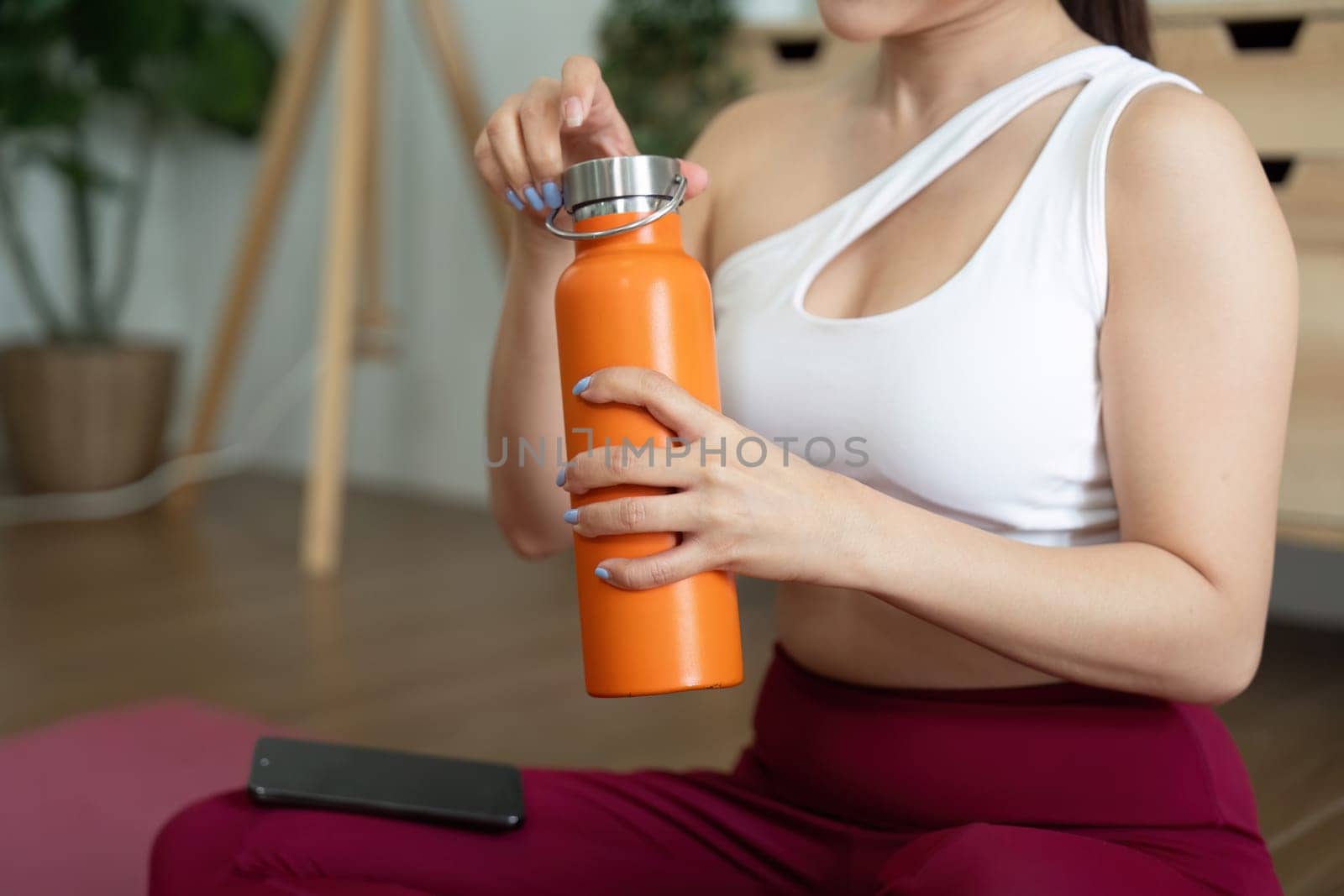 Focused on her wellness routine, a woman opens her brightly colored water bottle, ready to hydrate and energize post-exercise.