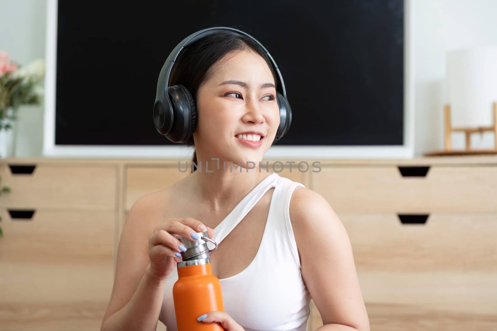 Focusing on wellness, a woman admires her orange water bottle, preparing to stay hydrated during her fitness regime.