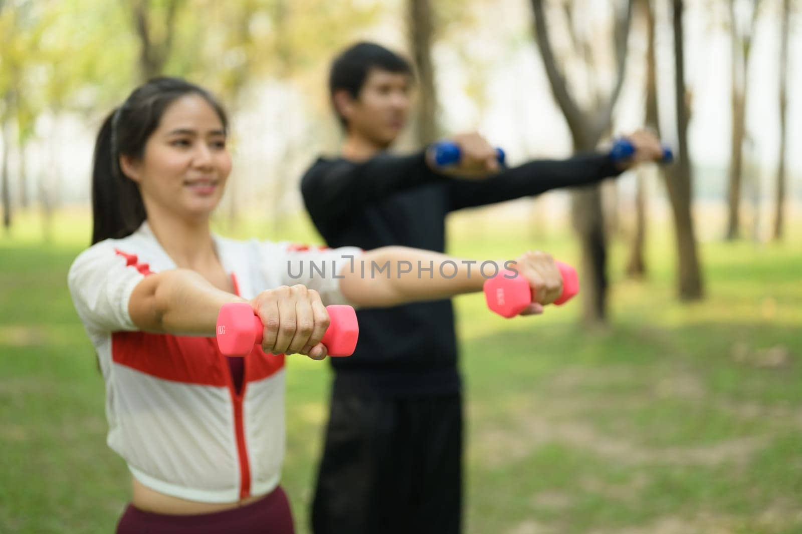 Young couple exercising with dumbbells in a peaceful park. Wellness and healthy lifestyle concept.
