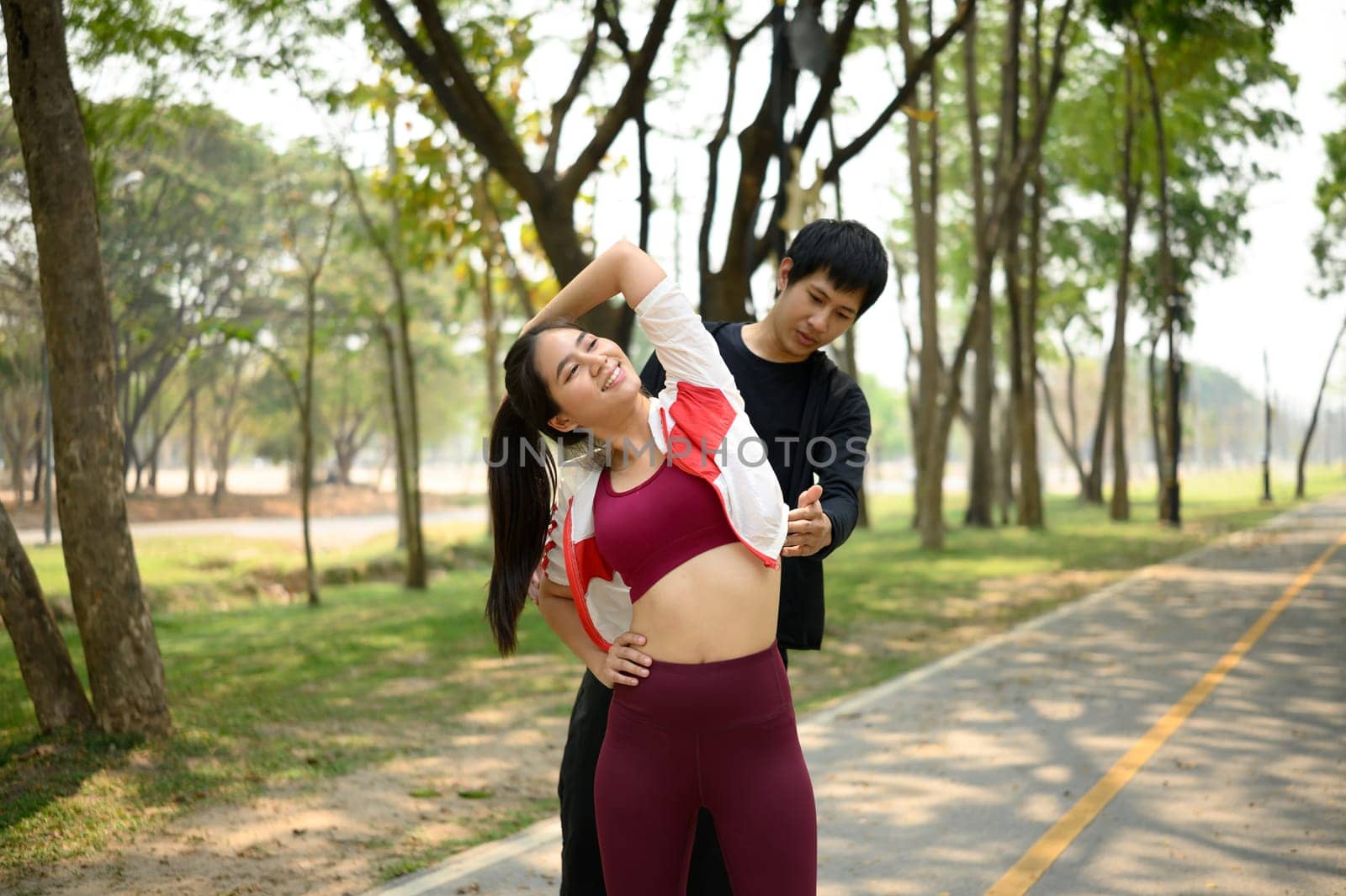 Young man assisting his partner stretching before run or workout on a peaceful path. Healthy lifestyle concept.