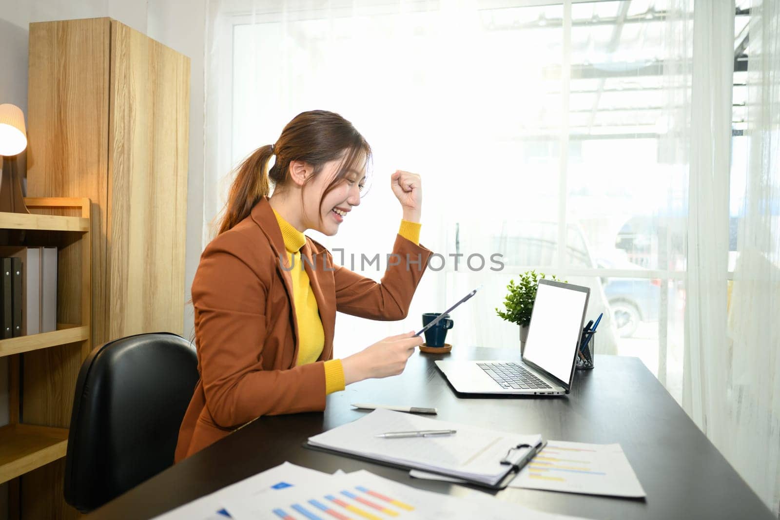 Excited businesswoman reading great news on digital tablet celebrating success in a bright workspace.