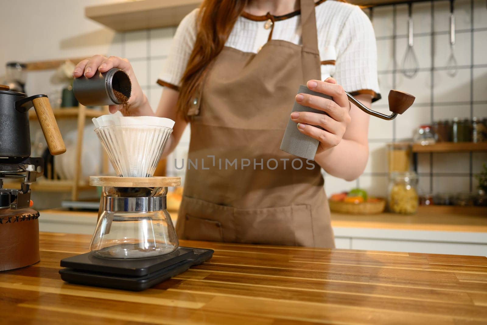 Close up of woman pouring freshly ground coffee into a filter cone for pour over brewing in a kitchen.