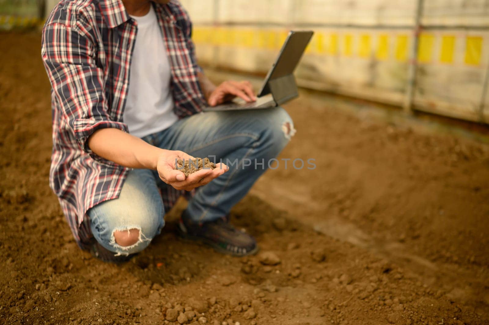 Agronomist holding a laptop and checking soil quality in an agricultural.