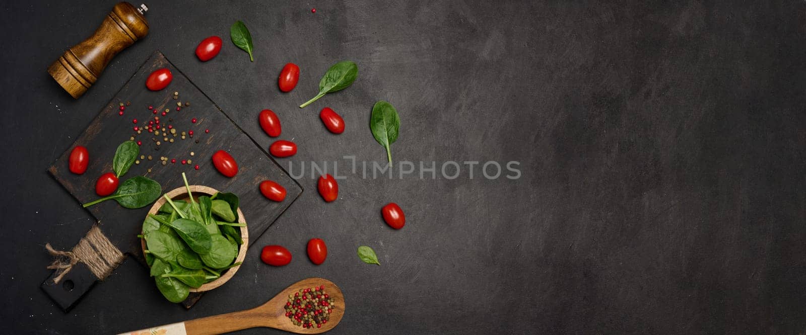 Fresh spinach leaves, cherry tomatoes, and mixed peppercorns on a black background. Copy space
